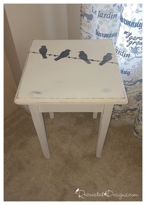 a rustic little table with birds sitting on a wire painted on it