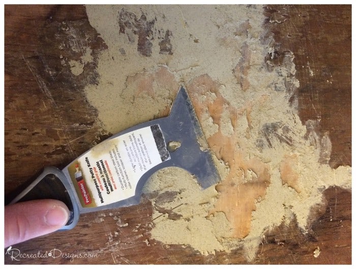 using a putty knife and wood filler to repair an old dresser