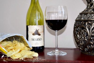 a bottle and glass of red wine and some potato chips