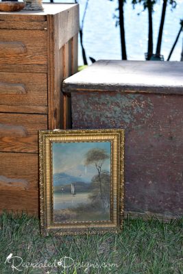an oil painting sitting against an antique trunk and some oak drawers