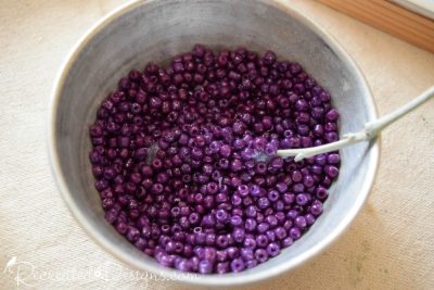 dipping a painted twigs into a bowl of purple beads and glitter