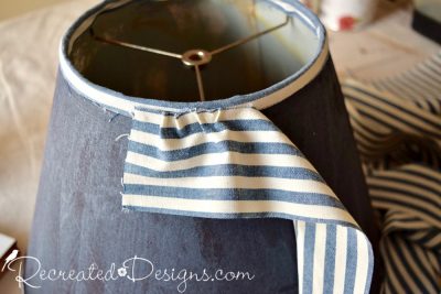 Attaching fabric to an old lamp shade by using hot glue to make ruffles