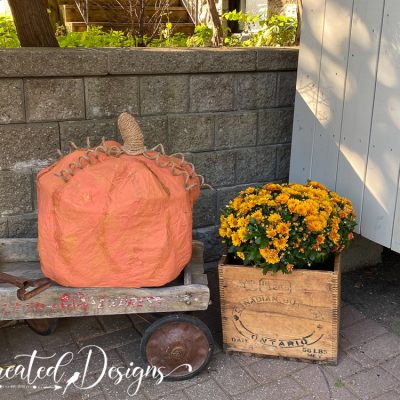 a giant paper mache pumpkin sitting on an old wagon next to some fall flowers