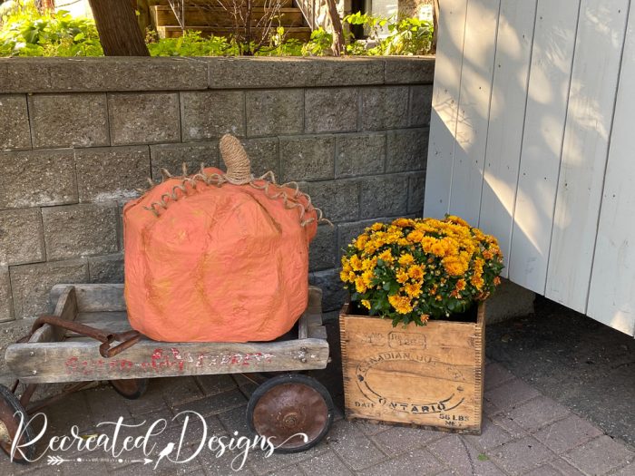 a giant paper mache pumpkin sitting on an old wagon next to some fall flowers