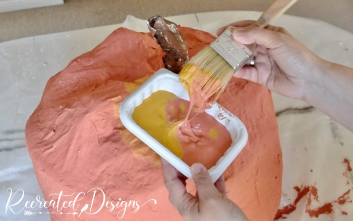 a paint brush dipped in orange and yellow paint to paint a giant pumpkin
